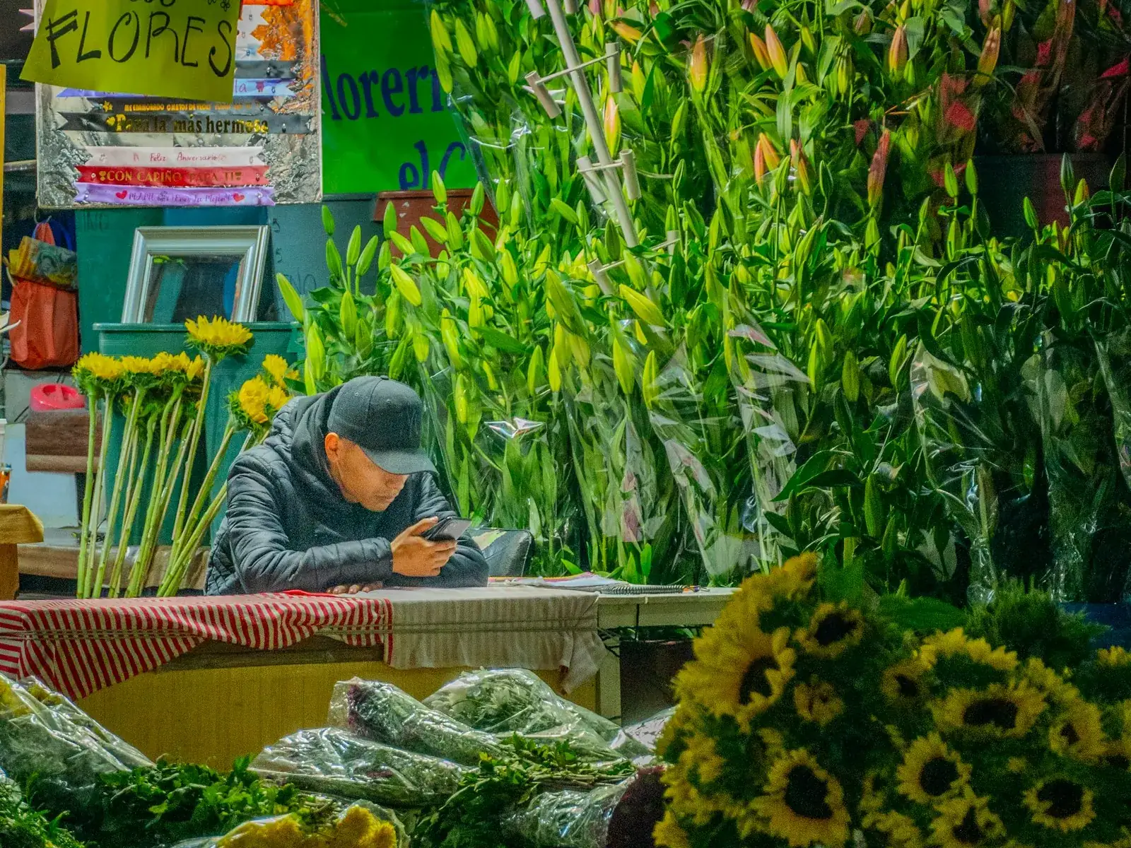 Un fleuriste, au marché, consulte son téléphone entre ses bouquets