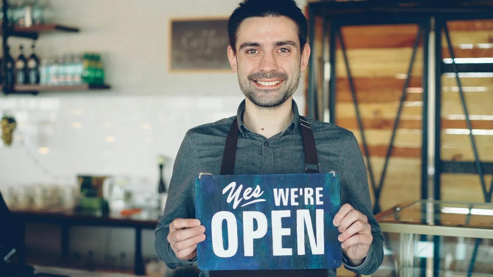 Un commerçant souriant tient une pancarte « open » devant son comptoir