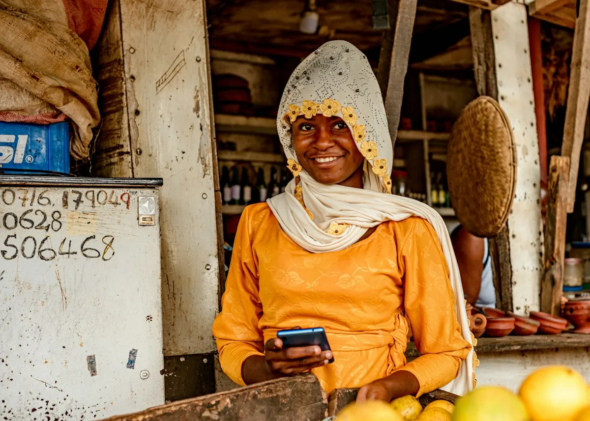 Une primeure souriante, téléphone en main, derrière ses fruits
